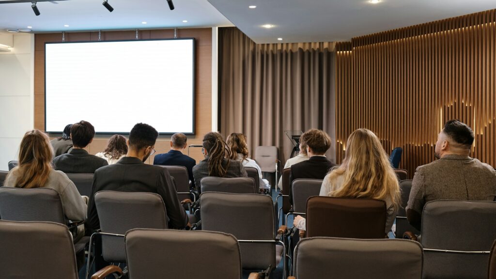 IAM-konferenssin osallistujia salissa seuraamassa esitystä.